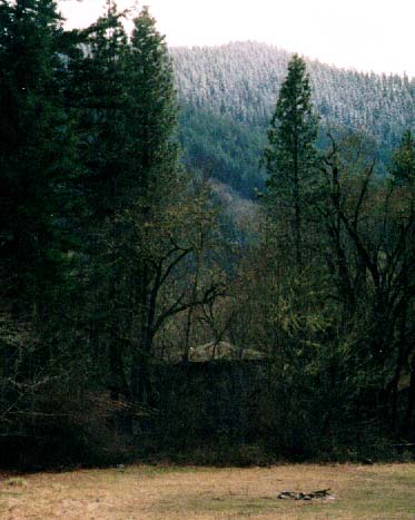 Trillium School sits in the trees south of the School Meadow. Snowy Trillium Mountain rises beyond the river.